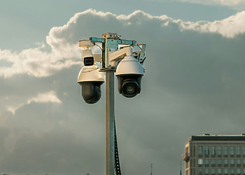 Multiple surveillance cameras mounted on a pole against a cloudy sky