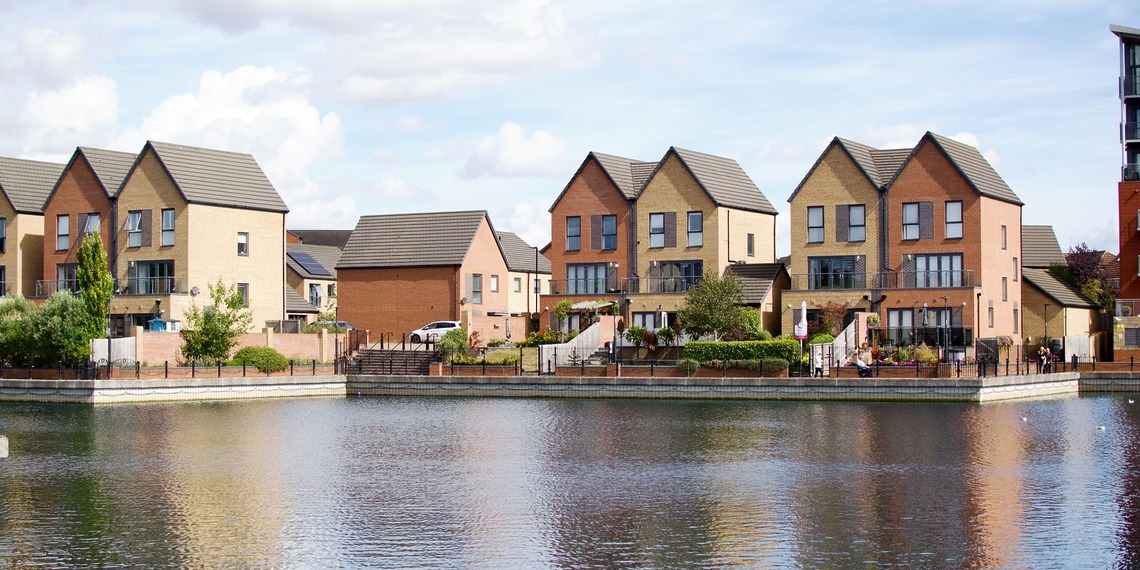 Row of modern houses by a lake with clear reflections and blue sky.