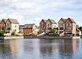 Row of modern houses by a lake with clear reflections and blue sky.