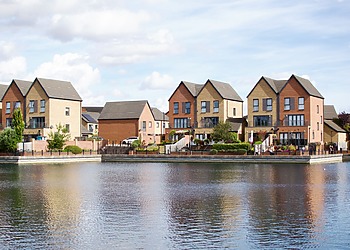 Row of modern houses by a lake with clear reflections and blue sky.