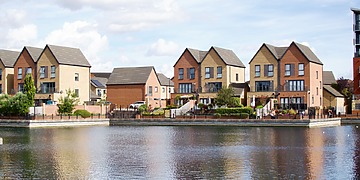Row of modern houses by a lake with clear reflections and blue sky.