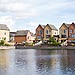 Row of modern houses by a lake with clear reflections and blue sky.