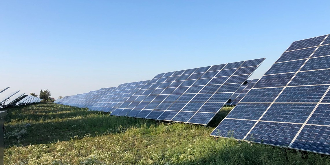 Solar panels in a green field under a clear blue sky in Tortona, Italy.