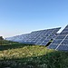 Solar panels in a green field under a clear blue sky in Tortona, Italy.