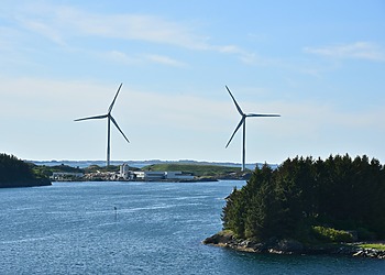 Two wind turbines along the Norwegian coastline near Haugesund, surrounded by the sea and green islands.