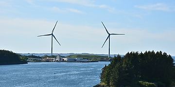 Two wind turbines along the Norwegian coastline near Haugesund, surrounded by the sea and green islands.