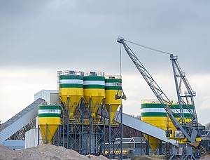 Industrial cement production facility with large storage silos and a crane.