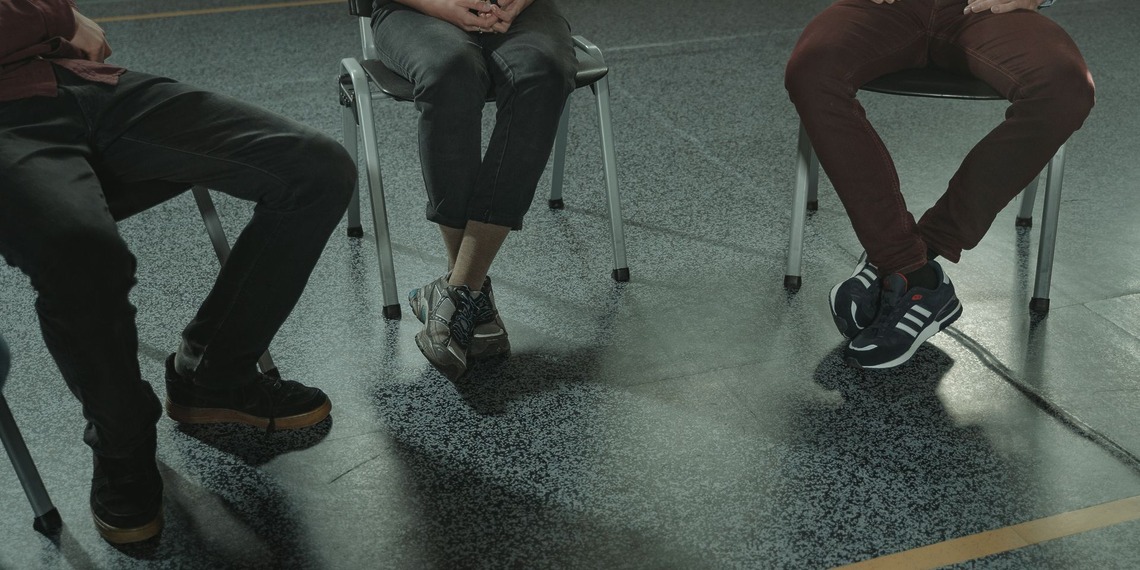 A group of three adults sitting in chairs during a discussion or support session indoors.