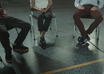 A group of three adults sitting in chairs during a discussion or support session indoors.