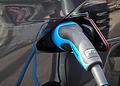 Blue and grey charge plug connected to a dark electric car.