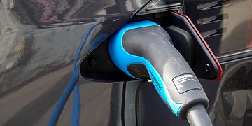 Blue and grey charge plug connected to a dark electric car.