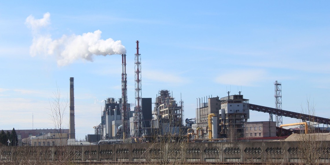 Industrial plant with tall chimneys and a white plume under a blue sky.