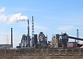 Industrial plant with tall chimneys and a white plume under a blue sky.