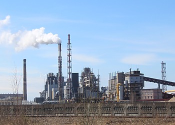 Industrial plant with tall chimneys and a white plume under a blue sky.