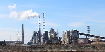 Industrial plant with tall chimneys and a white plume under a blue sky.