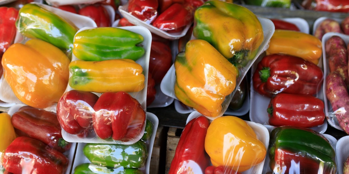 Vibrant assortment of packaged red, yellow, and green bell peppers at a market stall.