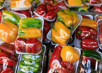 Vibrant assortment of packaged red, yellow, and green bell peppers at a market stall.