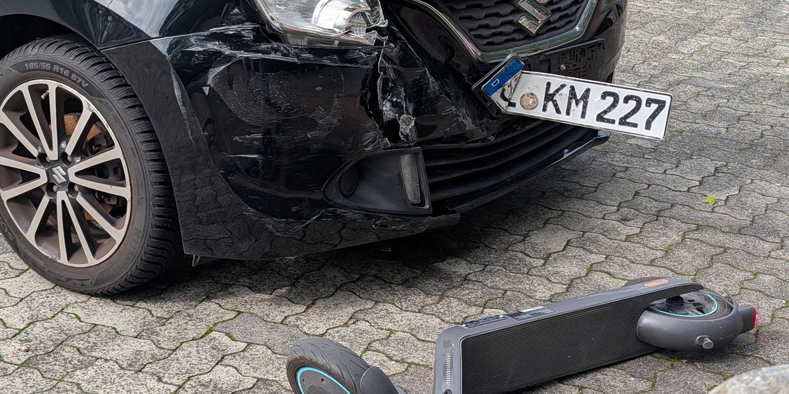 A damaged car and scooter after a collision in an urban setting.