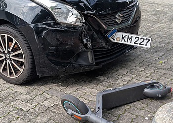 A damaged car and scooter after a collision in an urban setting.
