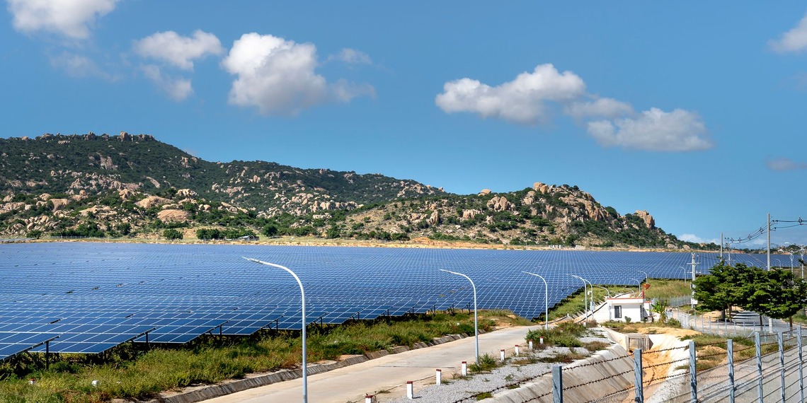 A vast solar farm with solar panels under a bright blue sky in the mountains.