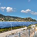 A vast solar farm with solar panels under a bright blue sky in the mountains.