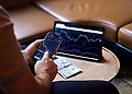 A person using a smartphone and tablet for stock market analysis, with graphs and cash visible.