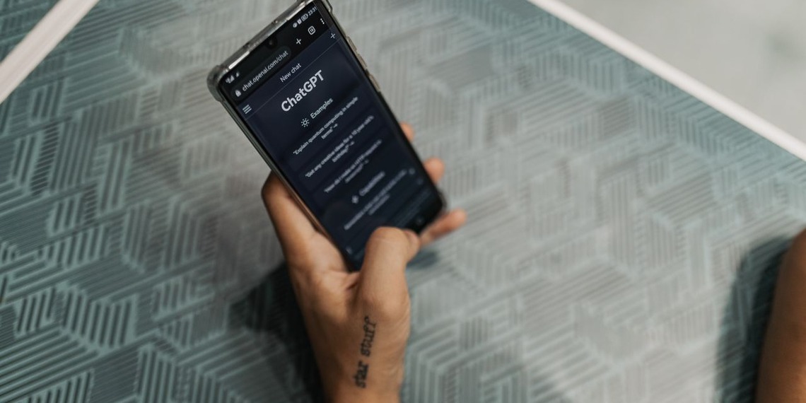 Close-up of a person holding a smartphone displaying the ChatGPT application interface on a patterned table.
