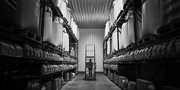 Rows of pressurized industrial refrigerant cylinders stored in a warehouse setting, representing the global chemical supply chain.