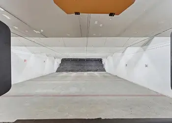 View down an empty indoor shooting lane toward the bullet trap, with numbered lanes on either side.