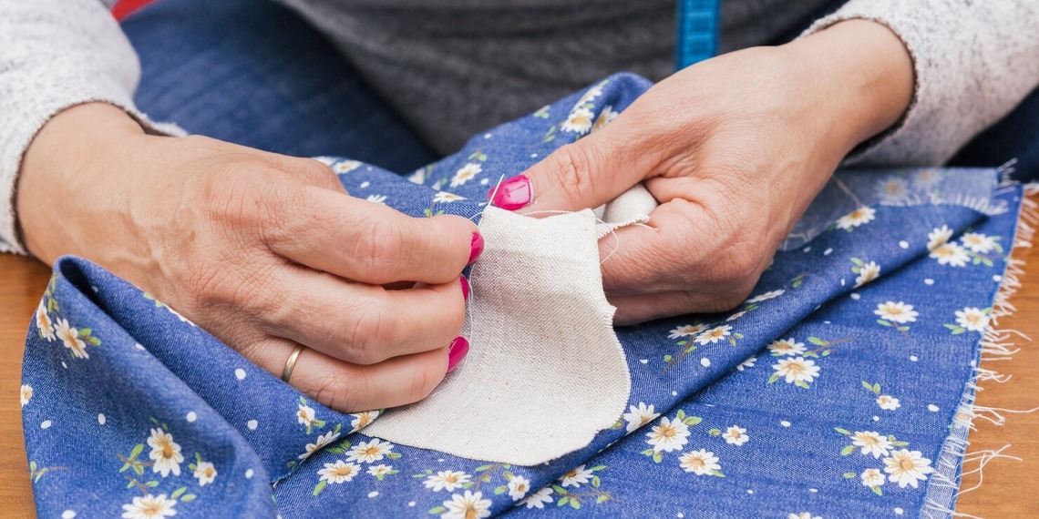 Hands sewing a contrasting patch onto blue floral fabric during a mending workshop