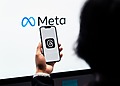 Meta logo displayed on a screen behind a person holding a phone.