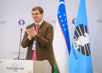 Timur Turlov standing beside the FIDE flag at the 2026 FIDE Congress in Samarkand